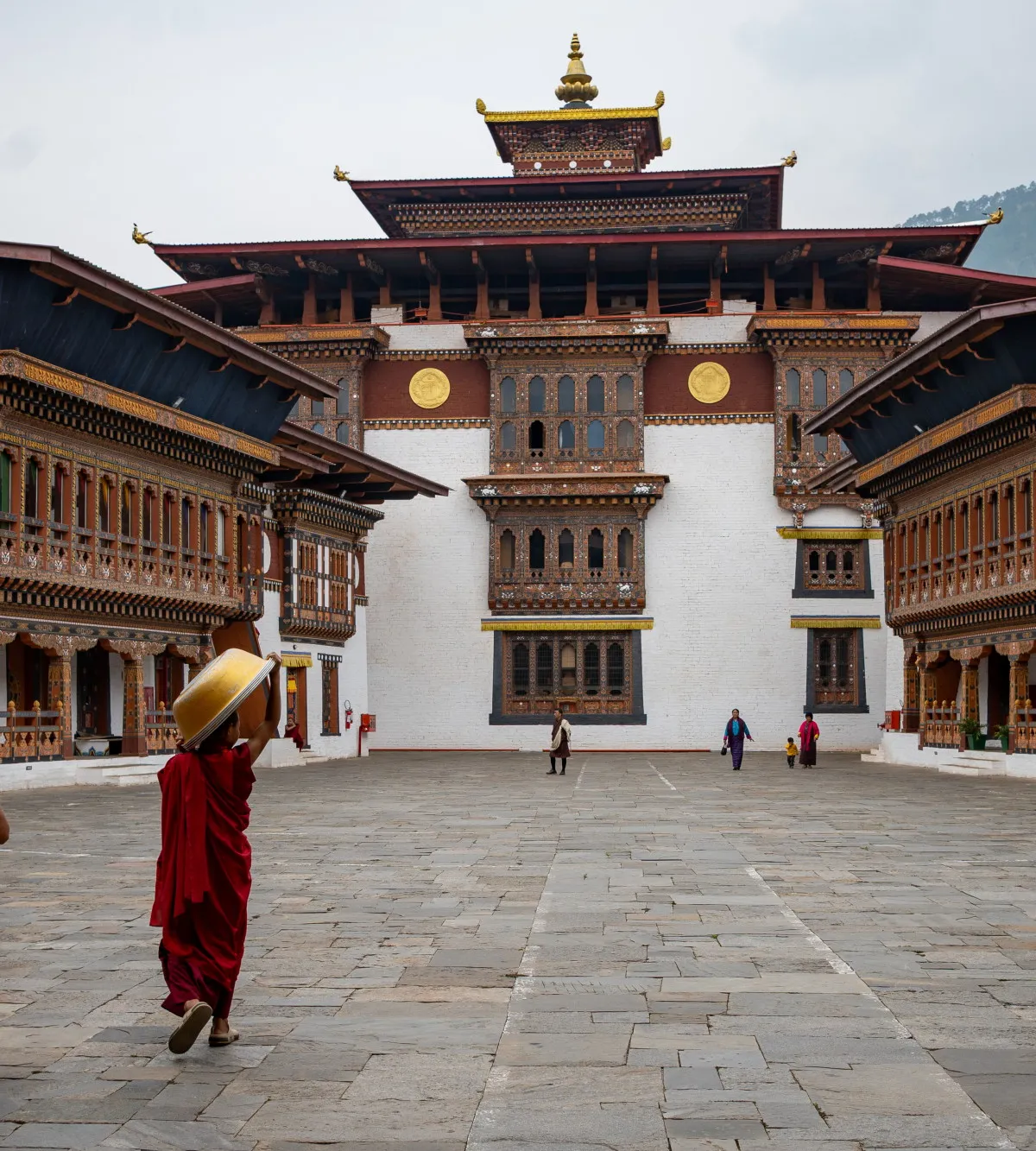 Two robed monks crossing the stone courtyard of Wangdue Phodrang Dzong with ornate painted woodwork, Bhutan