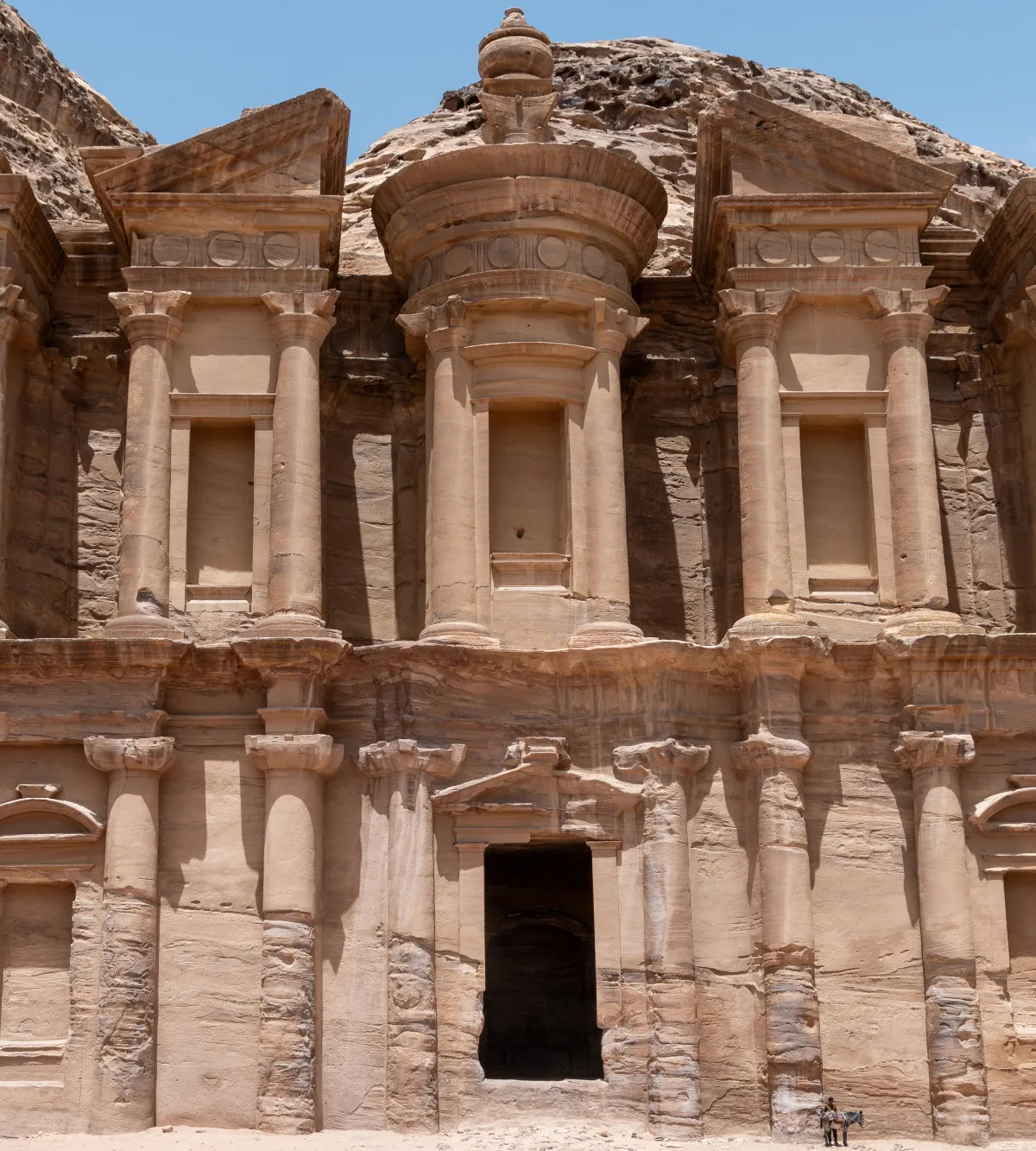 The towering Monastery (Ad Deir) facade with two donkeys resting at its base for scale, Petra, Jordan