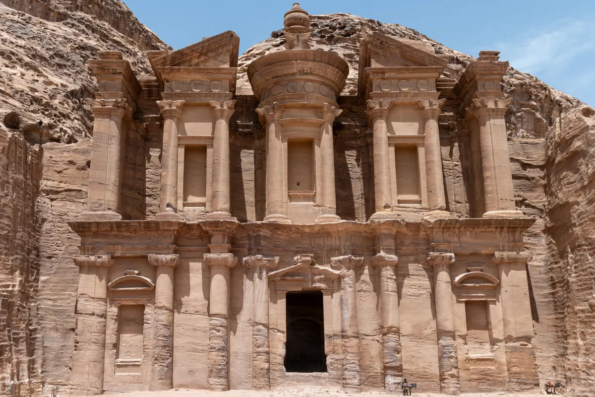The towering Monastery (Ad Deir) facade with two donkeys resting at its base for scale, Petra, Jordan