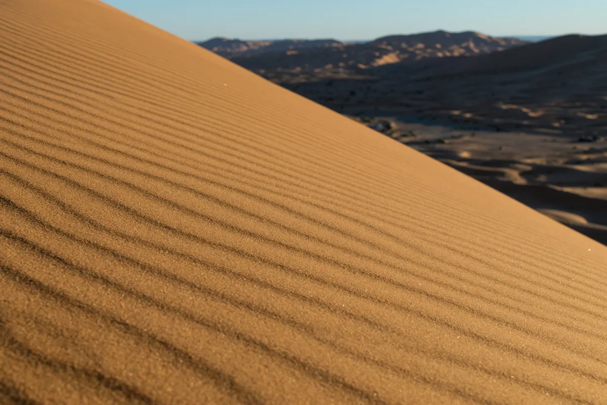 Close view of wind-rippled sand running diagonally down a desert dune with hills beyond, Rissani, Morocco