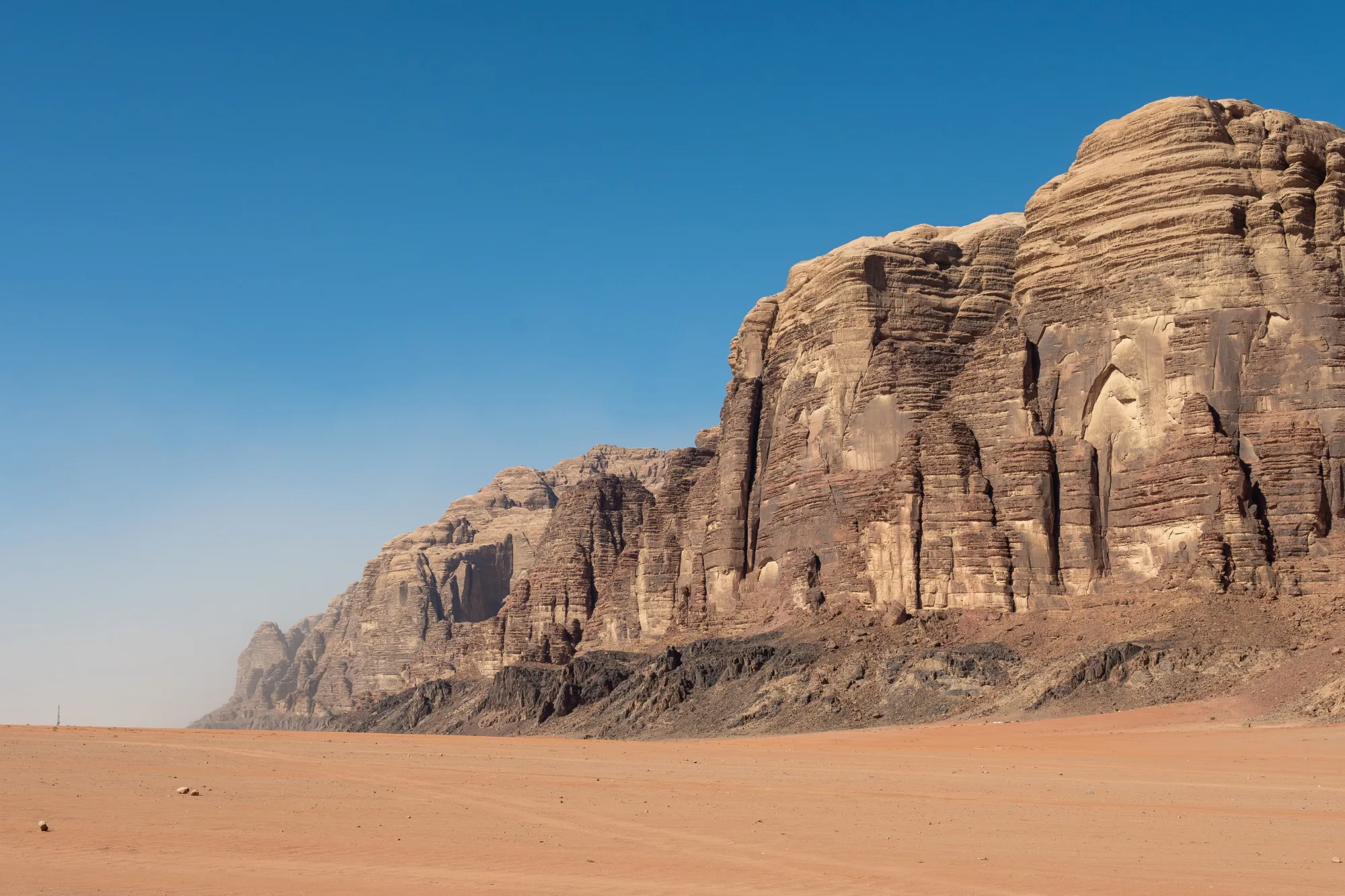 Layered sandstone massif rising from red desert under a deep blue sky, Wadi Rum, Jordan
