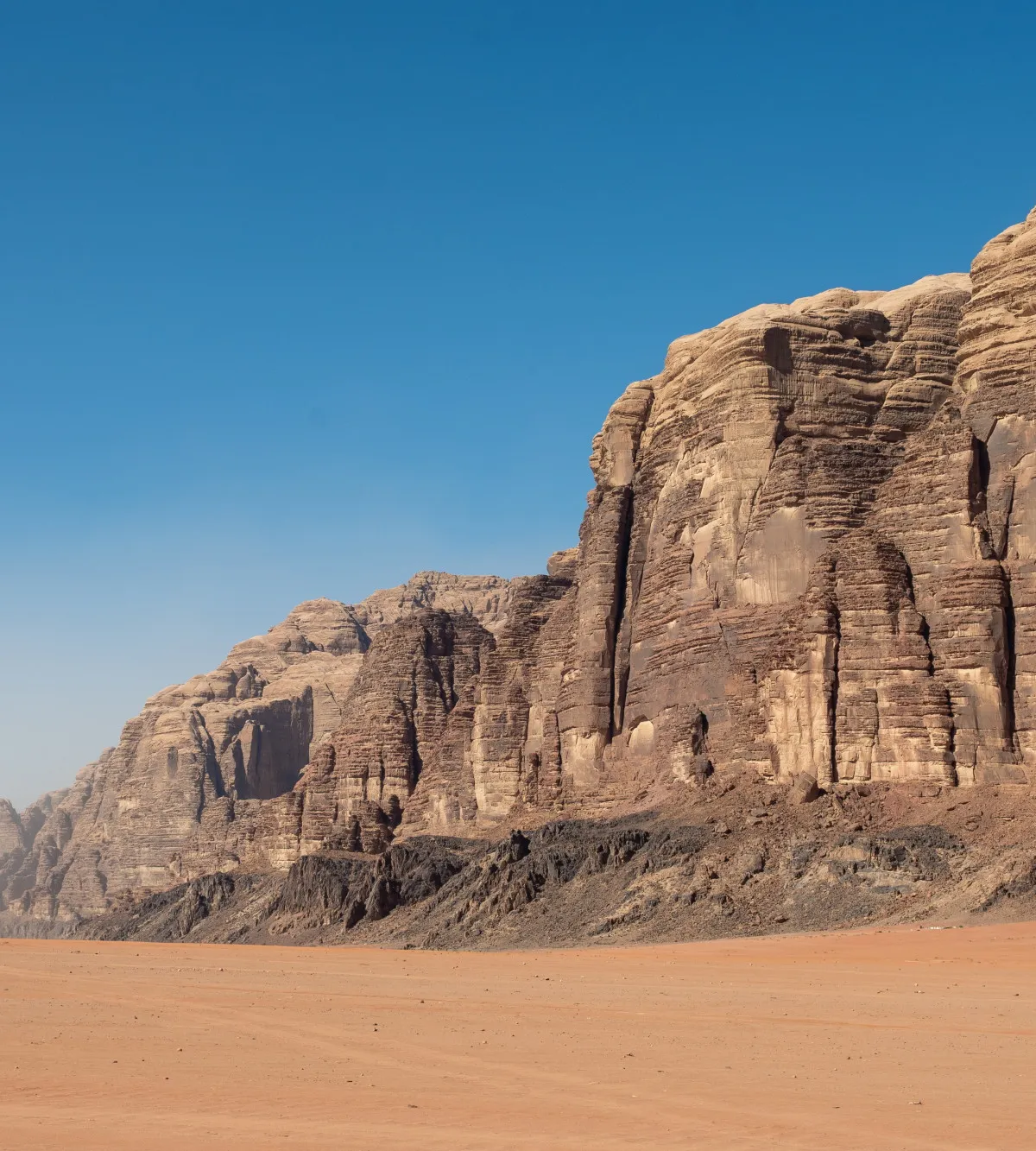 Layered sandstone massif rising from red desert under a deep blue sky, Wadi Rum, Jordan